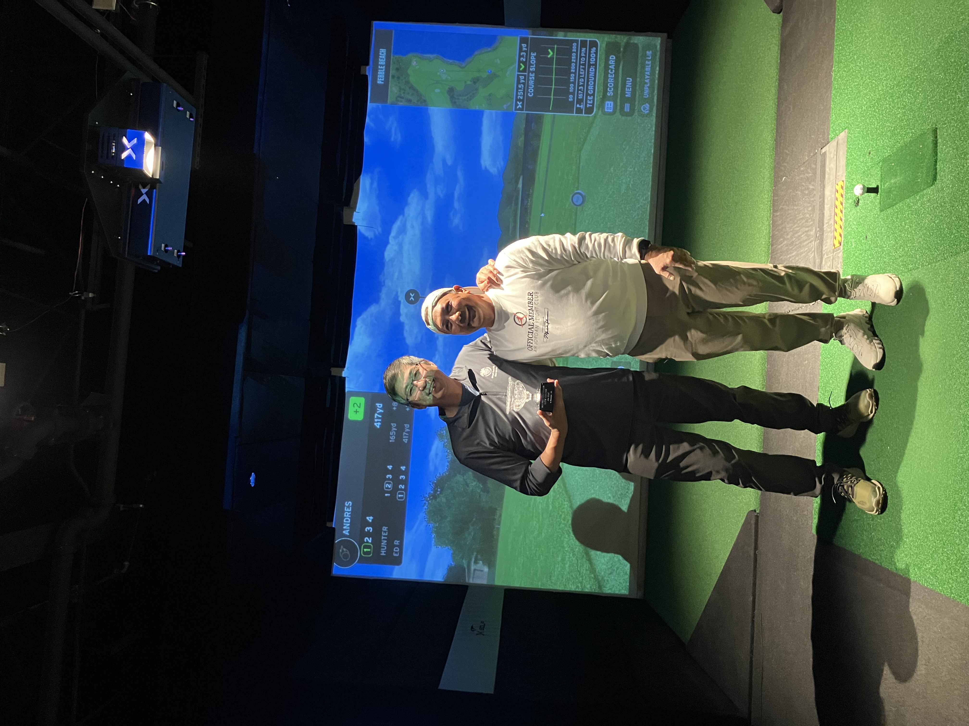 Two golfers in the simulator with a trophy